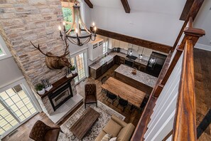 A spacious kitchen with a stone fireplace, a dining area with a wooden table and chairs, and a view of the outdoors through large windows.