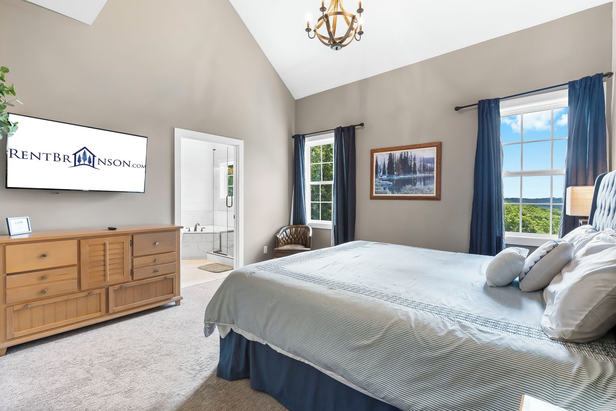 A bedroom with a large bed, a wooden dresser, a TV mounted on the wall, and a window with curtains.