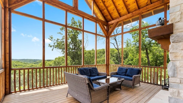 A covered outdoor area with wicker furniture and a stone fireplace.