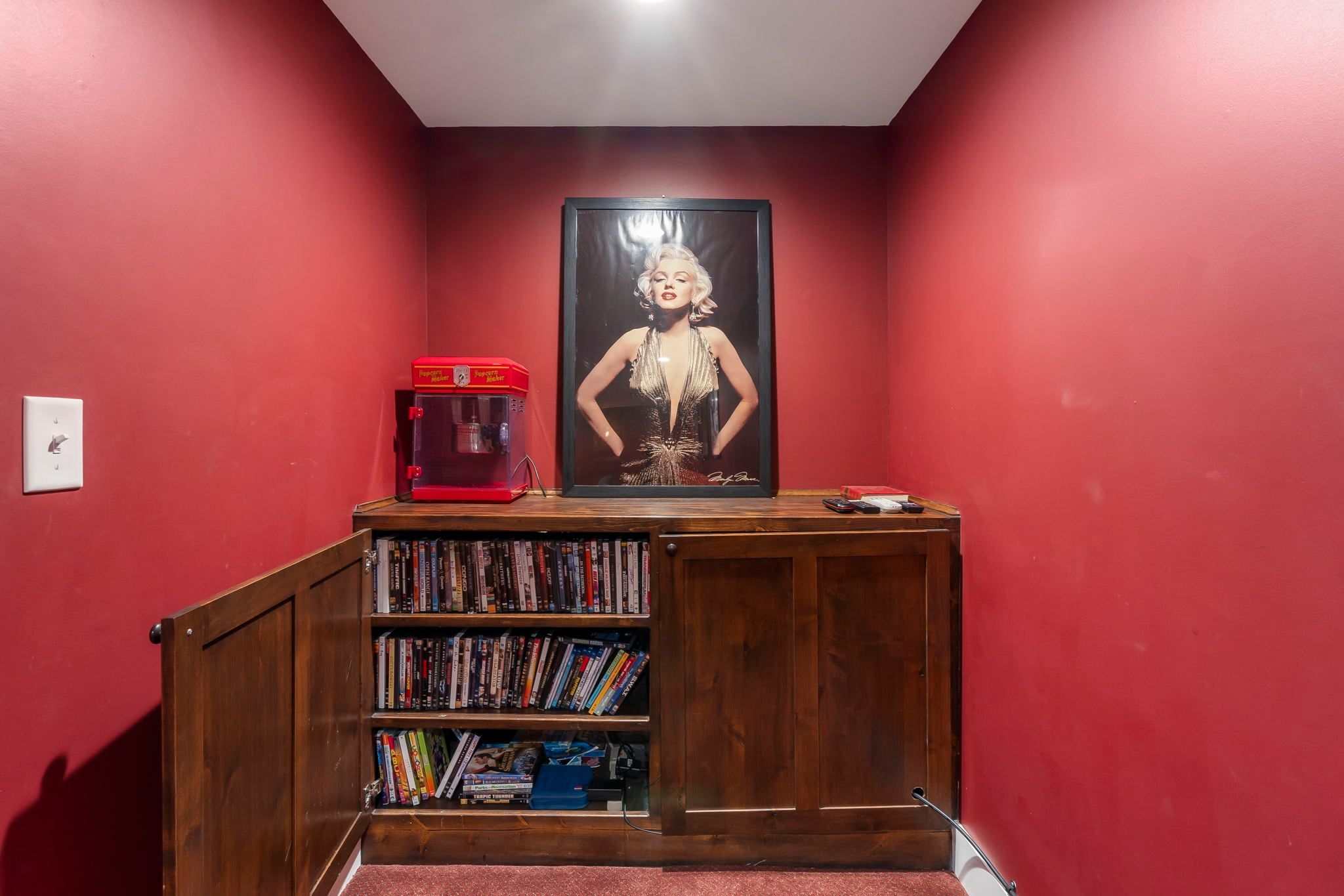 Un couloir aux murs rouges, une bibliothèque en bois remplie de livres, un appareil à pop-corn et un tableau encadré accroché au mur.