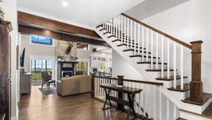 A spacious living area with a wooden staircase, a fireplace, and a view of the outdoors.