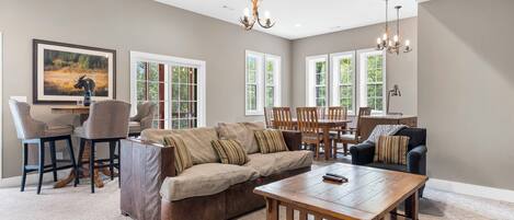 A spacious living room with a large sectional sofa, a coffee table, and a dining area with wooden chairs.