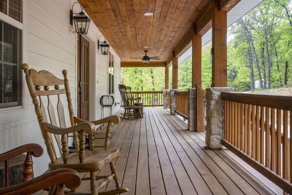 A wooden porch with rocking chairs and a stone pillar.