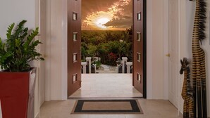 Un couloir donnant sur un coucher de soleil visible à travers une porte, avec une plante en pot et une statue de girafe.