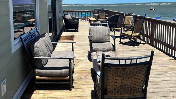 Een houten terras met rieten meubilair met uitzicht op een strand.