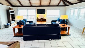 Een woonkamer met een hoge plafond, twee banken, een salontafel en een televisie. Ramen en een balkon zijn zichtbaar.