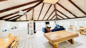 Ruime kamer met hoge plafonds, houten balken, een pooltafel en een eethoek met stoelen en een tafel.