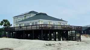 Een huis aan het strand met een houten terras en een overdekte ruimte.