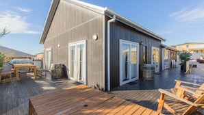 A wooden deck with outdoor furniture, a covered barbecue area, and a building with large sliding glass doors. - Oak & Barrell - 7 Twynam Street (Jindabyne)
