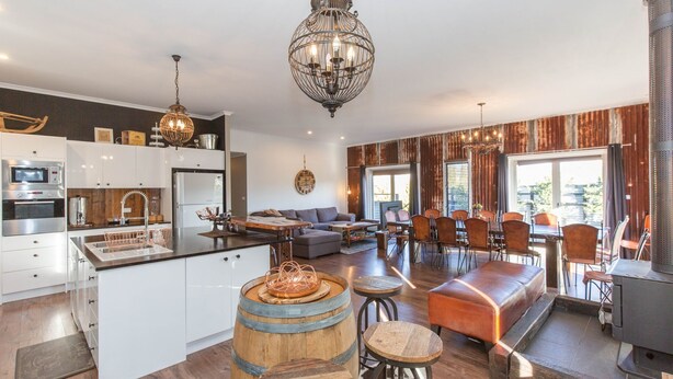 A modern kitchen with white cabinets, a central island, and a dining area with a wooden table and chairs. - Oak & Barrell - 7 Twynam Street (Jindabyne)