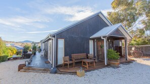 A rustic cabin with a wooden deck, outdoor seating, and a gravel driveway. - Oak & Barrell - 7 Twynam Street (Jindabyne)