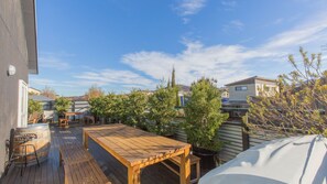 A wooden deck with a table and chairs, surrounded by potted plants and a barbecue grill. - Oak & Barrell - 7 Twynam Street (Jindabyne)