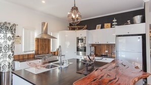 A modern kitchen with a central island, stainless steel appliances, and a wooden accent wall. - Oak & Barrell - 7 Twynam Street (Jindabyne)