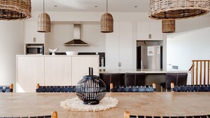A modern kitchen with a central island, hanging wicker pendant lights, and a dining area with a wooden table and chairs. - Escape 2 Brophy - Southern Ocean Views (Port Fairy)