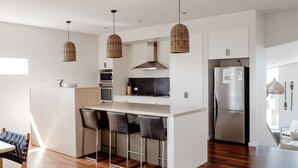 A modern kitchen with a central island, stainless steel appliances, and a dining area with bar stools. - Escape 2 Brophy - Southern Ocean Views (Port Fairy)