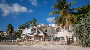 A beachfront property with a balcony overlooking the sea, a palm tree, and a white building with a balcony. - A Surfer's Home Away From Home! Soft round the edges, cozy and beachy (Oistins)