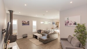 A modern living room with a fireplace, a sofa, a coffee table, and a dining area. - 43A Twynam Street - Spacious four bedroom home in central Jindabyne location (Jindabyne)
