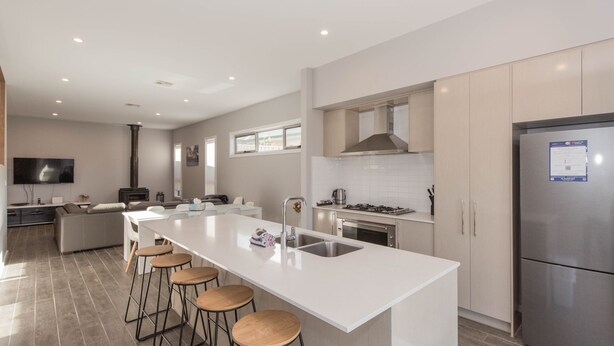 A modern kitchen with a large island, bar stools, a built-in oven, and a stainless steel refrigerator. - 43A Twynam Street - Spacious four bedroom home in central Jindabyne location (Jindabyne)