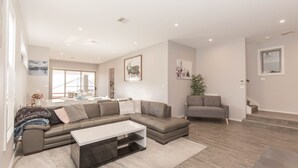 A modern living room with a sectional sofa, a coffee table, and a grey armchair. - 43A Twynam Street - Spacious four bedroom home in central Jindabyne location (Jindabyne)