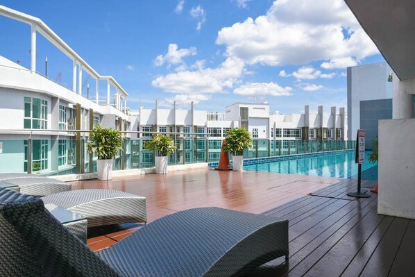 Relax on the rooftop terrace with a clear view of the pool, surrounded by lounge chairs and lush greenery.