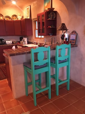 Uma cozinha com ilha central, duas cadeiras verde-água, armários vermelhos, micro-ondas, torradeira e pia.