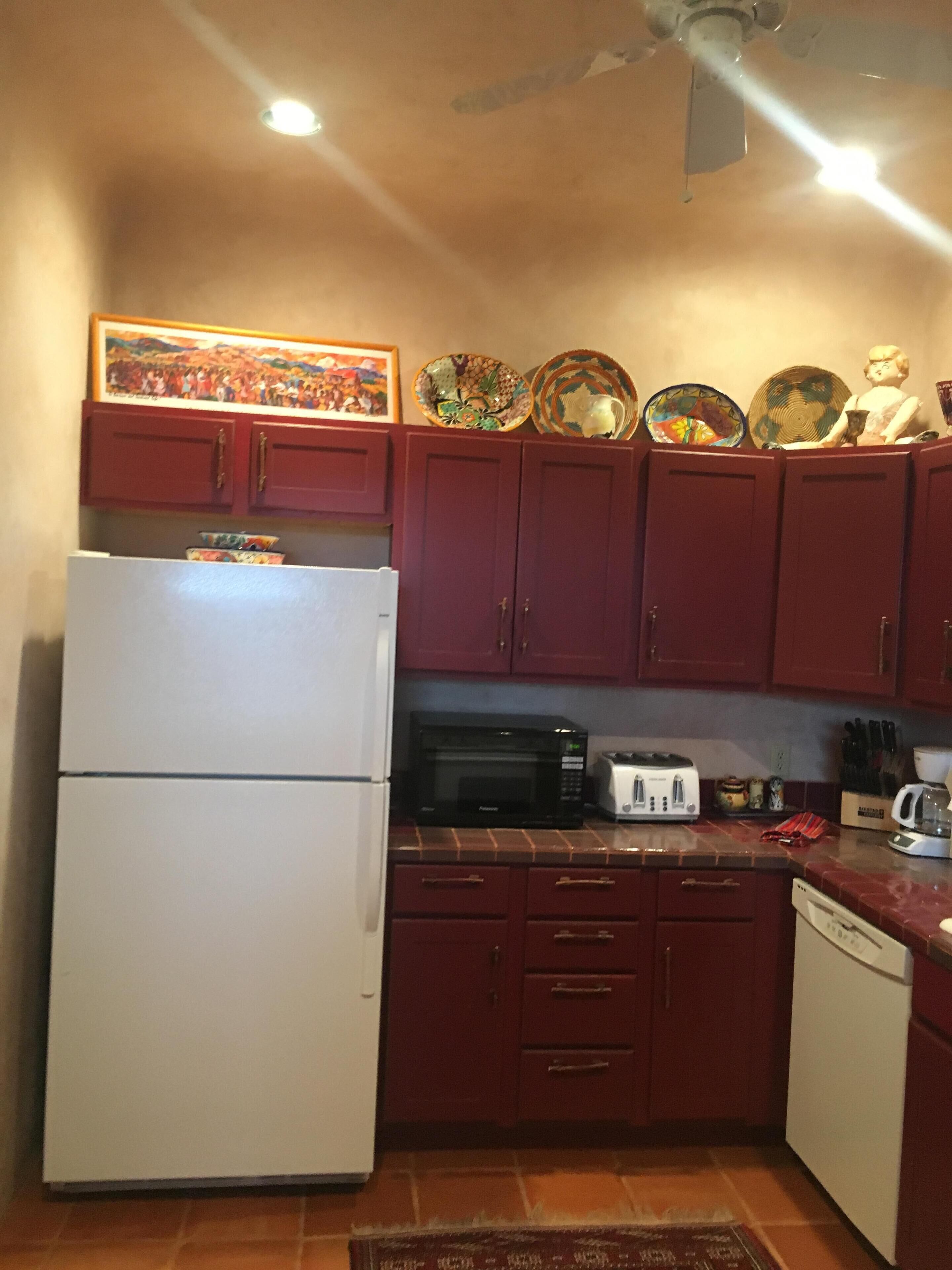 A compact kitchen with a white refrigerator, a microwave, a toaster, and a dishwasher. There are red cabinets and a tiled backsplash.