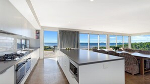 Una cucina moderna con una grande isola, un'area pranzo con mobili in vimini e vista sull'oceano.