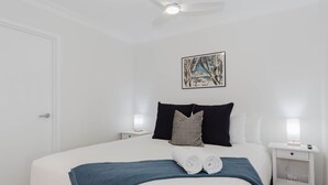 A hotel room with a bed, two bedside tables, a ceiling fan, and a painting on the wall.