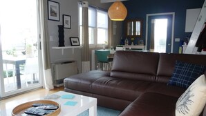Ein Wohnzimmer mit einem braunen Ledersofa, einem weißen Couchtisch und einem Korbtablett mit Fernbedienungen.