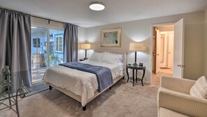 A bedroom with a bed, two bedside tables with lamps, a chair, a glass table with a decorative item, a window with curtains, and a door leading to another room. - Spacious Wine Country Home: 1 Mi to Downtown Lodi! (Lodi)