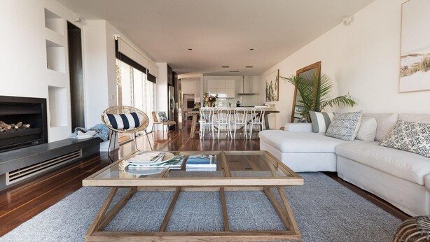 A modern living room with a glass coffee table, white sofa, and a fireplace. - Spinnakers Waterfront (Port Fairy)