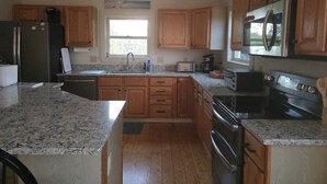 A kitchen with wooden cabinets, granite countertops, a stainless steel refrigerator, a microwave, a toaster, and a stove.