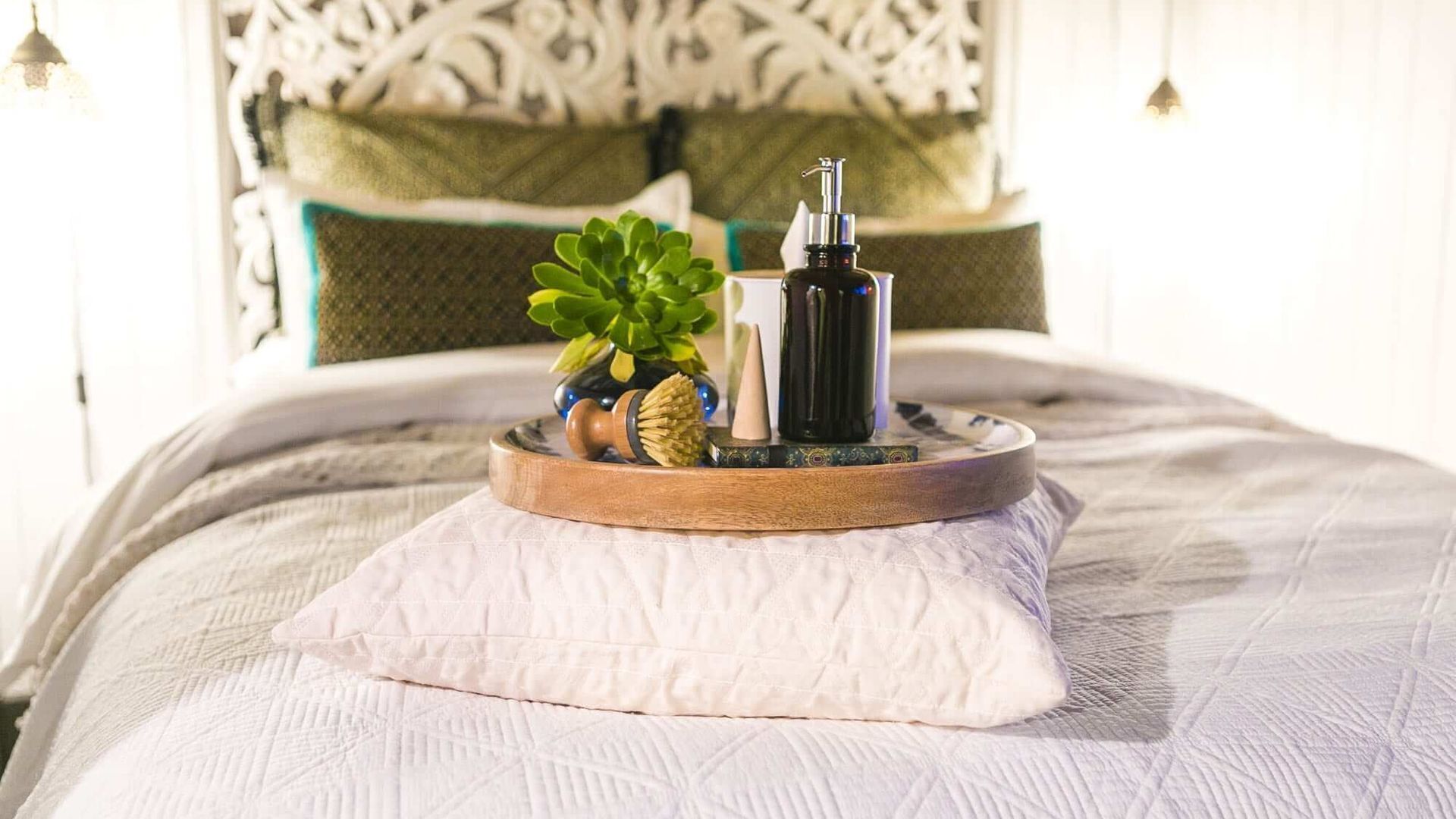 A neatly made bed with a decorative tray holding a plant, a candle, and a bottle.