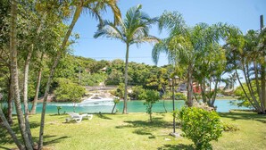 A tropical landscape with a clear view of a boat docked near a body of water, surrounded by lush greenery and palm trees. - Casa Quinta da Margem (Florianópolis)