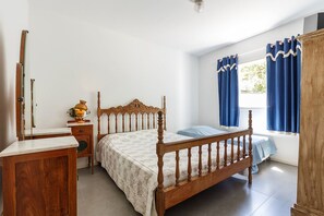 A bedroom with a wooden bed, a bedside table, a mirror, and a window with curtains. - Casa Quinta da Margem (Florianópolis)