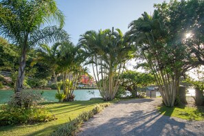 A gravel path leading to a body of water, surrounded by lush greenery and palm trees. - Casa Quinta da Margem (Florianópolis)
