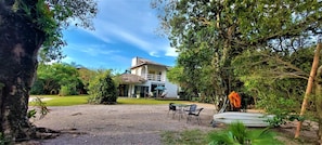 A house with a gravel driveway, a lawn, and a patio area with chairs and a table. - Casa Quinta da Margem (Florianópolis)