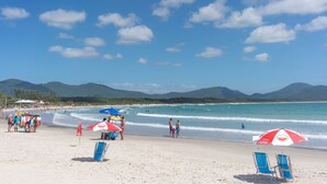 A beach with clear skies, a few people, and beach umbrellas. - Casa Quinta da Margem (Florianópolis)