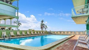 Una piscina con sillones de descanso, un patio de ladrillo y un cielo despejado.