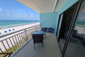 A balcony with a table and chairs, a view of the beach, and a sliding glass door leading to an interior space with a chair and a table. - Chateaux Condominium 404-Breathtaking gulf views! (Indian Shores)