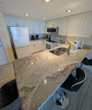 A kitchen with white cabinets, a granite countertop, stainless steel sink, and a built-in oven. - Chateaux Condominium 404-Breathtaking gulf views! (Indian Shores)
