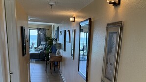 A hallway with a wooden floor, a rug, framed pictures, and a dining area with a table and chairs. - Chateaux Condominium 404-Breathtaking gulf views! (Indian Shores)