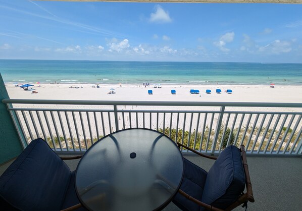 A balcony with a glass table and chairs, overlooking a beach with several sun loungers and people. - Chateaux Condominium 404-Breathtaking gulf views! (Indian Shores)