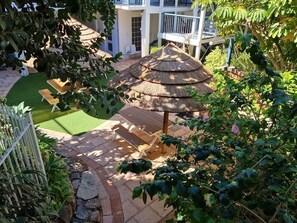 A courtyard with a thatched-roof gazebo, a wooden bench, and a small lawn area. - West Beach  Lagoon 107 - Great Value (Scarborough)