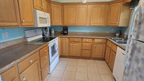 A kitchen with wooden cabinets, a white stove, a microwave, and a refrigerator.