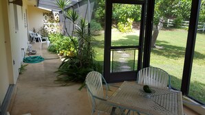 A covered patio with a table and chairs, surrounded by potted plants and a view of a grassy yard.