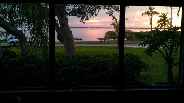 A view of a lake with a sunset, trees, and a parked car.