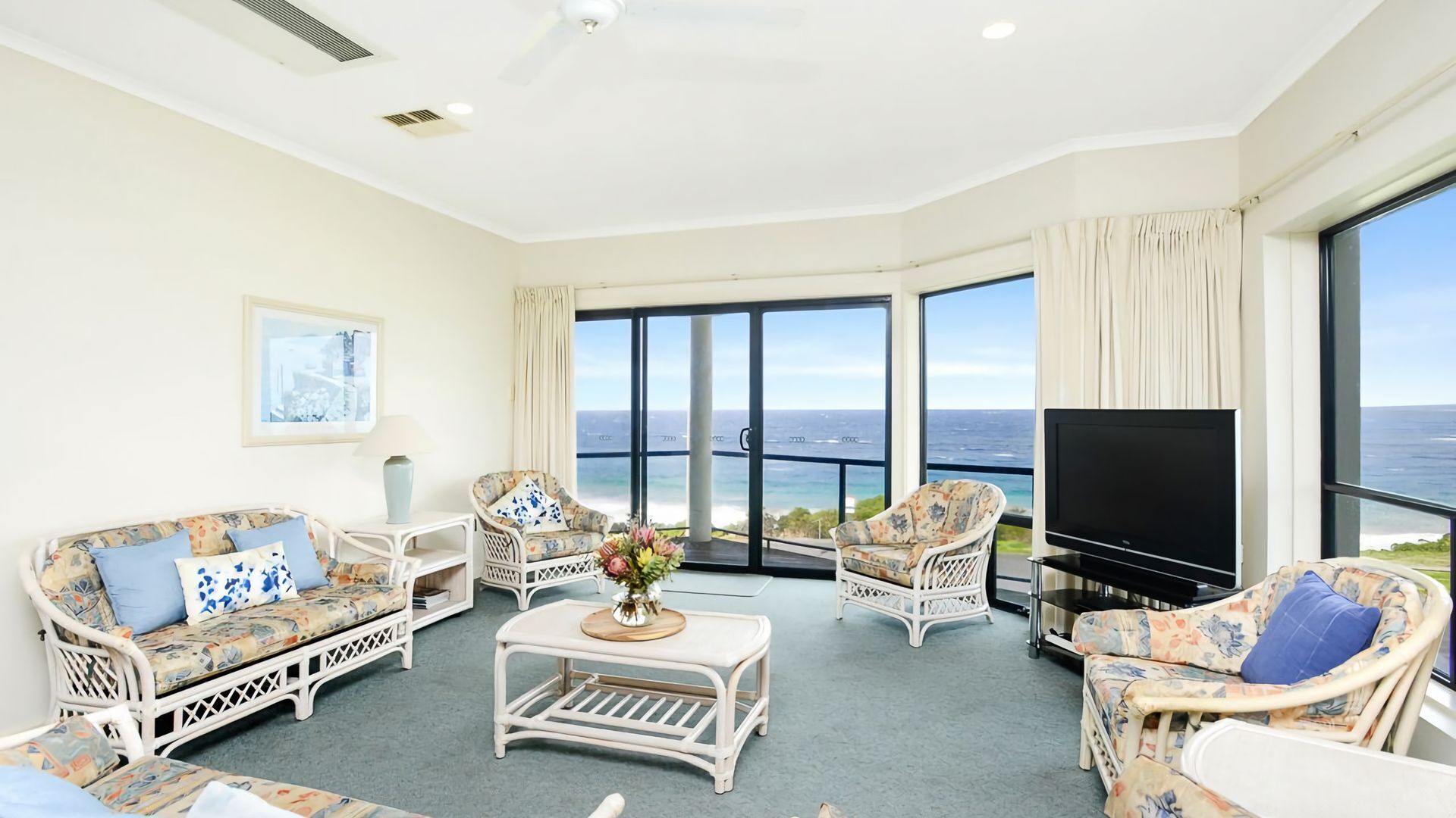 A spacious living room with a large TV, comfortable seating, and a view of the ocean.