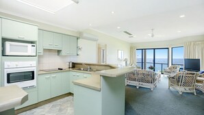 A modern kitchen with built-in appliances, a dining area with wicker furniture, and a balcony with a view of the sea. - Million Dollar Sea Views (Hayborough)