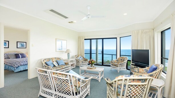 A spacious living room with a large TV, wicker furniture, a ceiling fan, and a view of the ocean. - Million Dollar Sea Views (Hayborough)